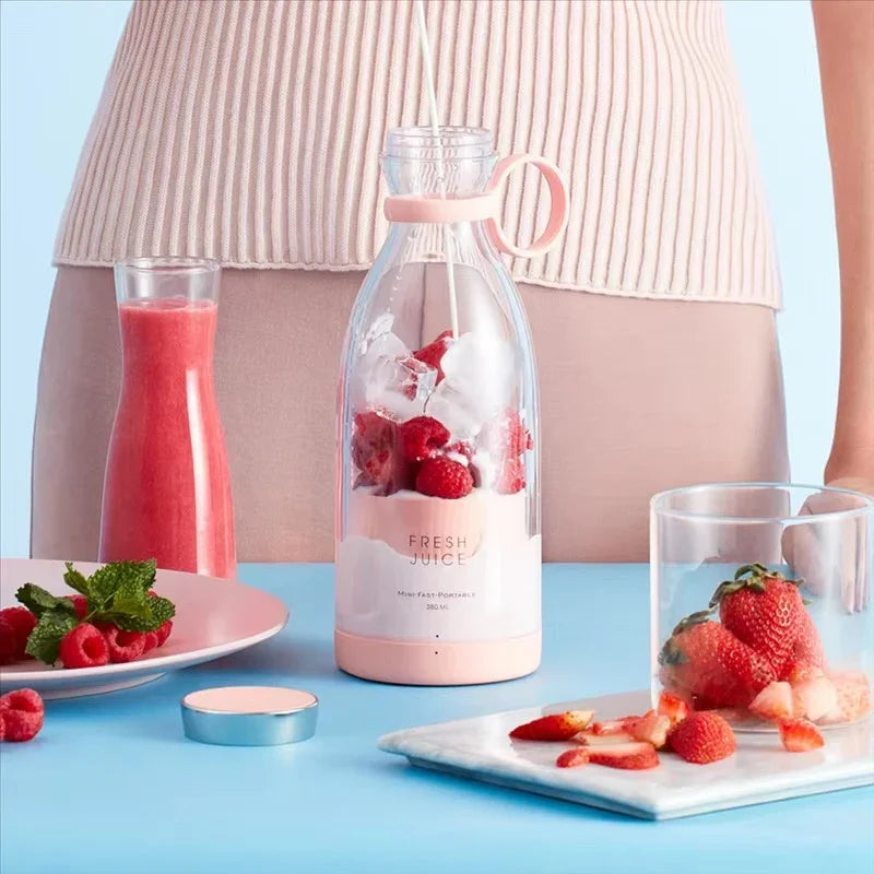 Licuadora portátil rosa con fresas, frambuesas y hielo, junto a jugo rojo y frutas frescas sobre mesa azul